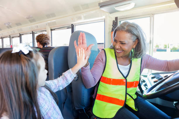 Female driver high-fives student boarding school bus As a young schoolgirl boards the school bus, the female bus driver gives her a high-five. school bus driver stock pictures, royalty-free photos & images
