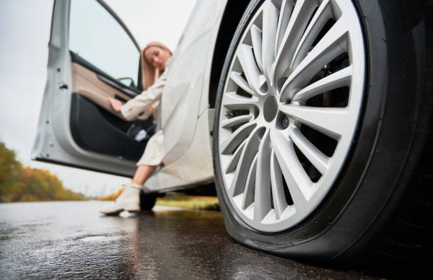 Female driver of white car observing punctured tire on rear wheel. stock photo