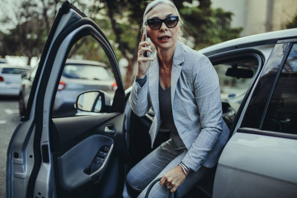 Female entrepreneur travelling to office in a luxurious car Senior businesswoman getting out of a car talking on phone. Female entrepreneur travelling to office in a luxurious car. open car door stock pictures, royalty-free photos & images