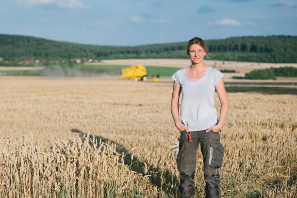agricultrice se tenant dans le champ de blé, moissonneuse-batteuse à l’arrière-plan - portrait agriculteur photos et images de collection