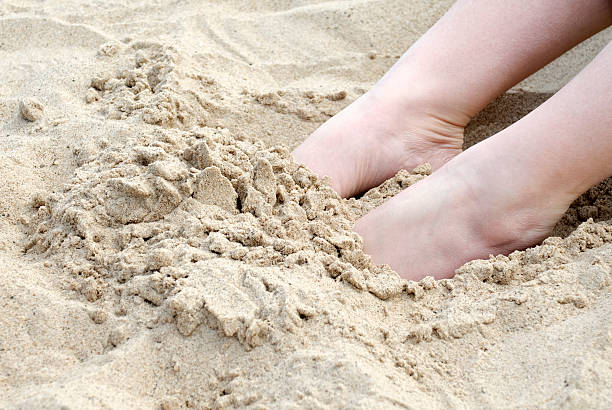 Female Feet Buried in Sand at the Beach Female feet buried in the sand at the beach. human feet buried in sand. summer beach stock pictures, royalty-free photos & images