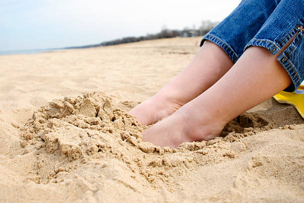 Female Feet Buried in Sand at the Beach Female feet buried in the sand at the beach with an overcast sky in the background. human feet buried in sand. summer beach stock pictures, royalty-free photos & images