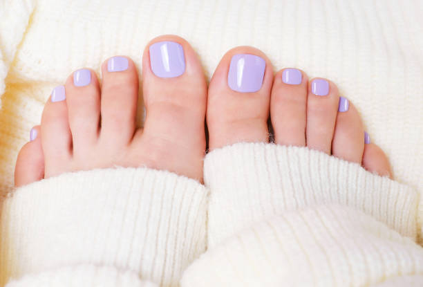 Female feet with purple pedicure on white knitted surface, top view. stock photo