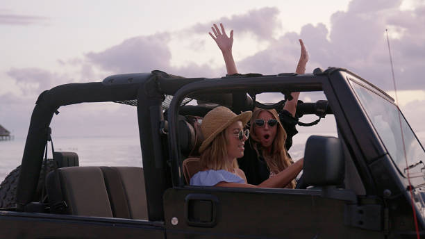 Female friends escaping to the idyllic beach. Looking through SUV window, opening arms stock photo