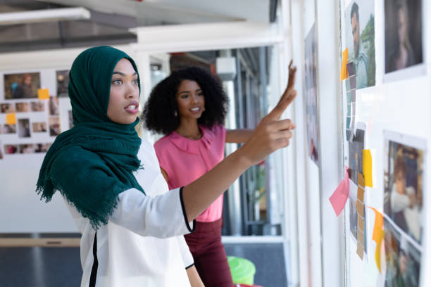 vrouwelijke grafisch ontwerpers die over foto's in office discussiëren - islam stockfoto's en -beelden