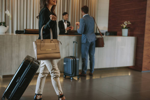 Female guest walks inside a hotel lobby Female guest walks inside a hotel lobby with people in the background at reception counter. Woman arriving at hotel. hotel reception photos stock pictures, royalty-free photos & images