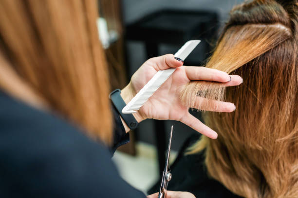 Female hairdresser is cutting woman hair close up. Female hairdresser is holding in hand between fingers a red hair is cutting woman hair close up. cutting hair stock pictures, royalty-free photos & images