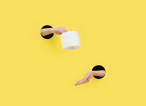 A female hand gives toilet paper on a yellow background. Hand in a paper hole. Help concept. stock photo