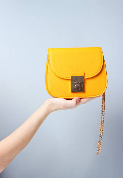 borsa femmina in pelle gialla alla moda con catena dorata su sfondo grigio. - borsetta foto e immagini stock