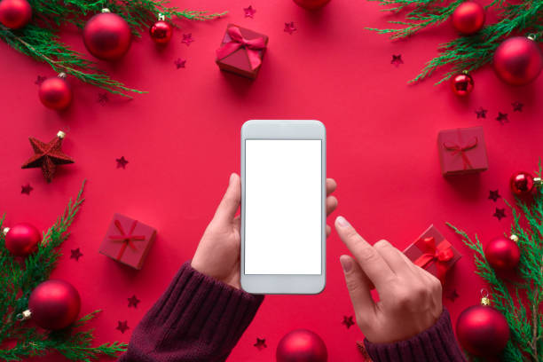 female hand hold phone on merry christmas red background, girl customer shopper using online mobile shopping app choosing holiday gifts with mobile payments on mock up white screen, close up top view - smartphone christmas imagens e fotografias de stock