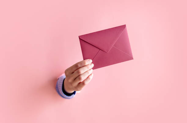female hand hold red envelope on pink background. stock photo
