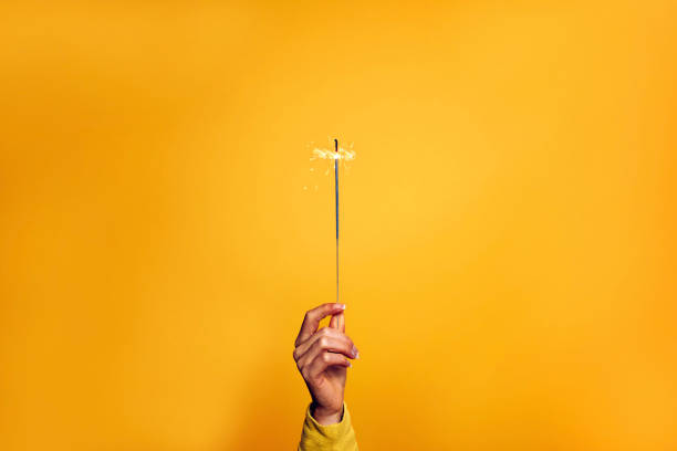 Female hand holding a sparkler light on a yellow background - Christmas, new year, birthday and celebration concept stock photo