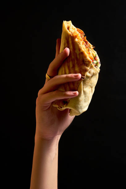 Female hand holds shawarma with red sauce, meat and vegetables on a dark background stock photo
