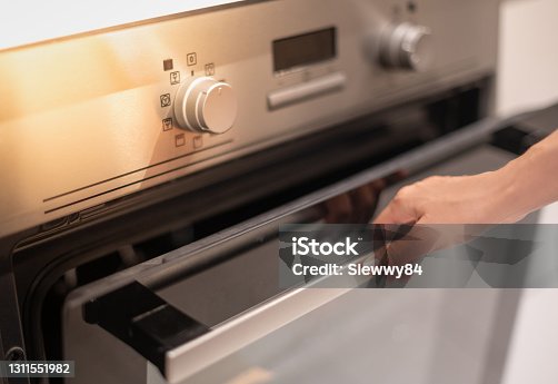 istock Female hand professional cook opening electric oven, while preparing dinner at home. Hobby, lifestyle. 1311551982