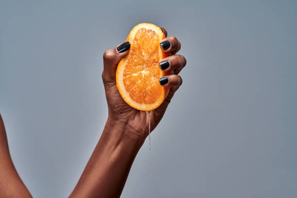 Female hand squeezing orange isolated on grey Female hand squeezing orange isolated on grey. Copy space crushed stock pictures, royalty-free photos & images