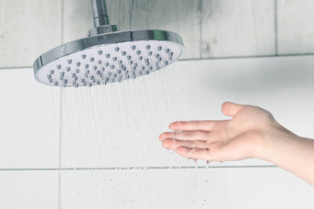 mano femminile che tocca l'acqua versando da un soffione della pioggia, controllando la temperatura dell'acqua - doccia foto e immagini stock