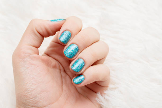 Female hand with blue nail design. Glitter blue nail polish manicure. Woman hand on white flyffy background. stock photo