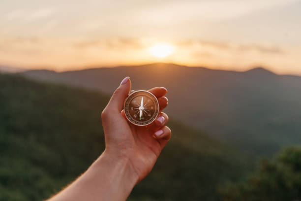 Female hand with compass in summer mountains at sunrise, pov. Explorer young woman holding compass in hand in summer mountains at sunrise, point of view. Concept of hiking and travel. compass stock pictures, royalty-free photos & images