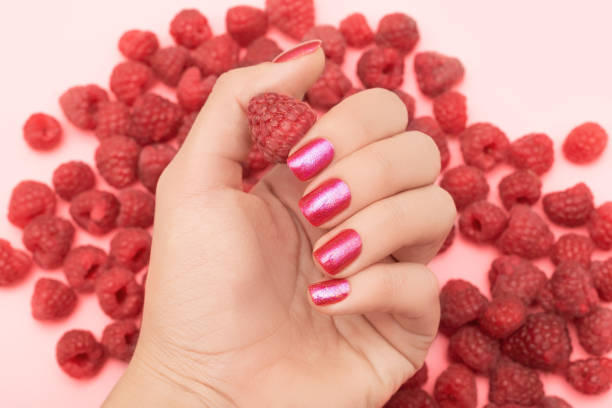 Female hand with glitter pink nail design. Female hand hold red ripe raspberry. Woman hand on red raspberries background stock photo