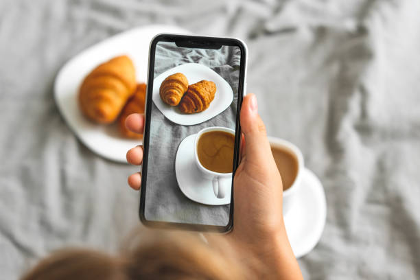 Female hand with mobile phone taking picture of tasty breakfast coffee and croissants in bed, closeup Female hand with mobile phone taking picture of tasty breakfast coffee and croissants in bed, closeup breakfast photos stock pictures, royalty-free photos & images