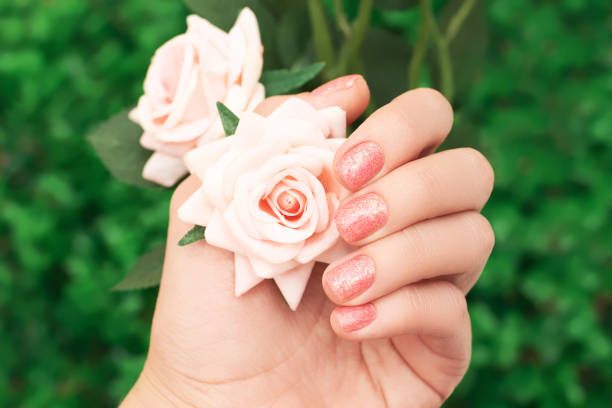 Female hand with orange nail design. Female hand hold pink rose flowers. Glitter orange nail polish manicure. stock photo