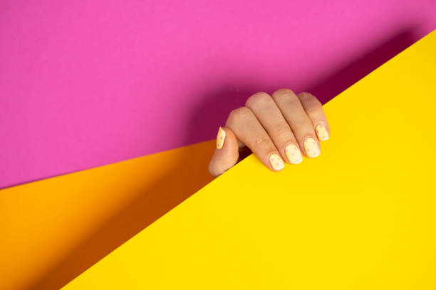Female hand with pastel yellow manicure on pink and orange background. stock photo
