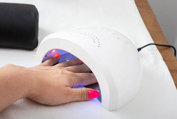 Female hand with pink nails in the lamp for manicure stock photo