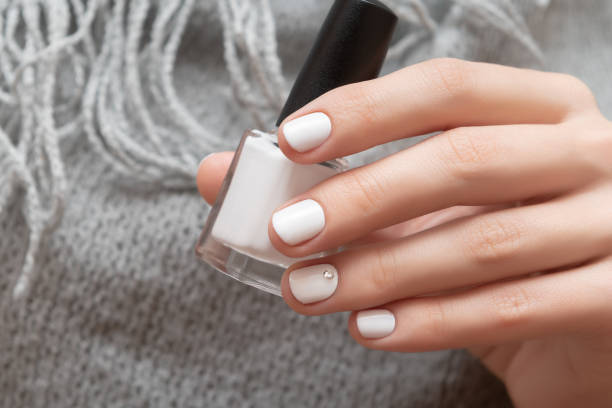 Female hand with white nail design holding nail polish bottle. stock photo