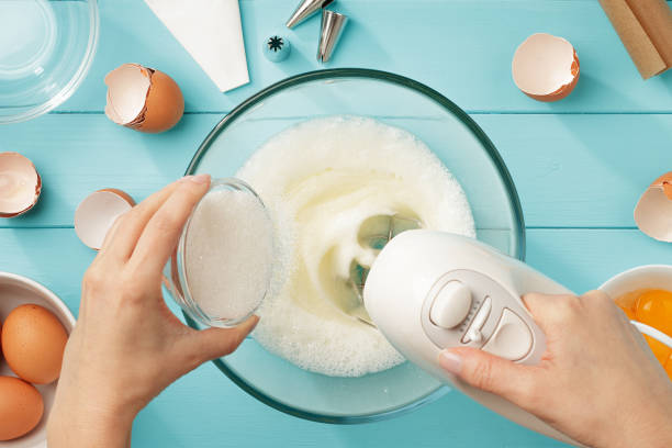 Female hands add a sugar to the bowl with whipping egg whites with mixer. Female hands add a sugar to the bowl with whipping egg whites with mixer on blue wooden table. Step by step recipe of meringue cookies. Top view. pavlova dessert photos stock pictures, royalty-free photos & images
