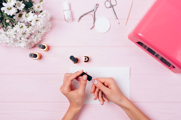Female hands apply shellac during manicure procedure Female hands apply shellac during manicure procedure, flat lay. Woman painting her nails with gel nail polish near UV lamp, tools and bouquet, view from above. painting fingernails stock pictures, royalty-free photos & images