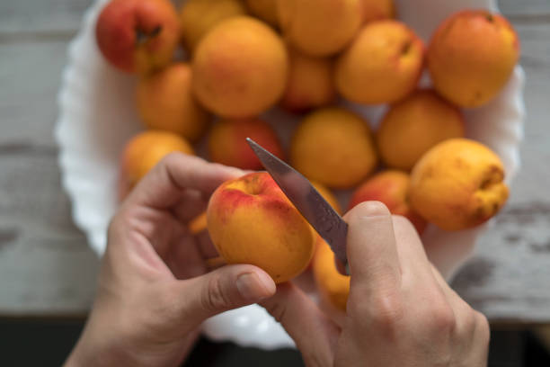 женские руки нарезают свежие сладкие персики, чтобы сделать персиковое варенье. - mitrovic стоковые фото и изображения