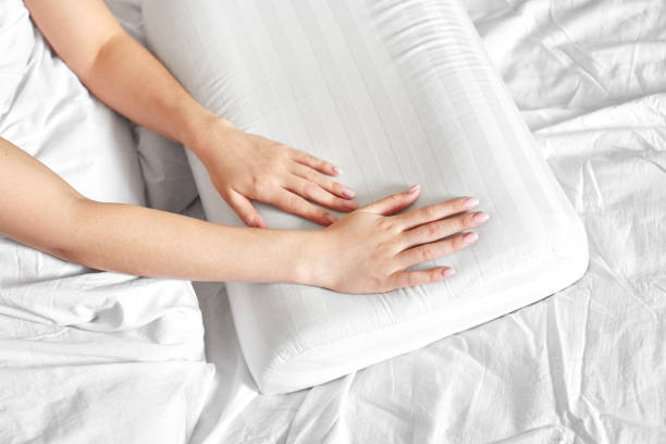 Female hands hold and show an orthopedic pillow on a white bed. Comfortable sleep and healthy spine stock photo