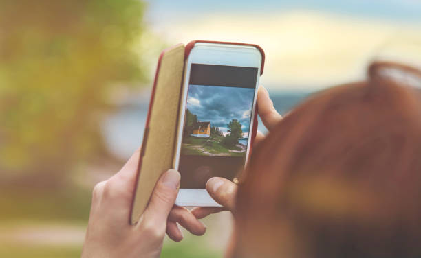 女性手拿著智慧手機, 同時在挪威的日落燈光下拍攝風景。 - oslo shooting 個照片及圖片檔