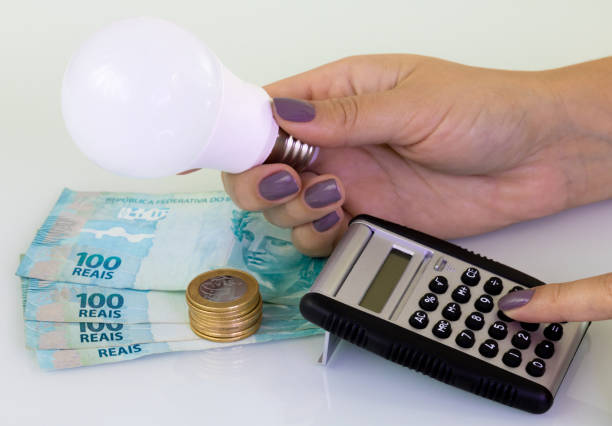 Female hands holding a lamp and typing a calculator. Real hundred brazilian notes and real one coins on white background. stock photo