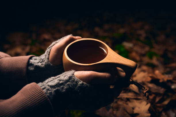 female hands holding a wooden national mug Kuksa with hot tea in the autumn forest at night stock photo
