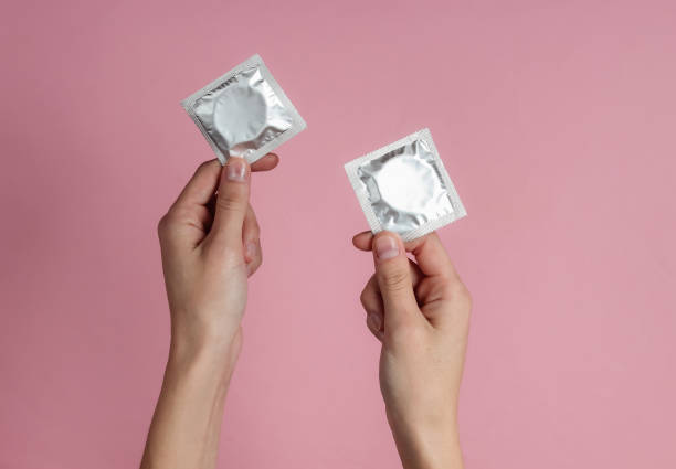 Female hands holding condom on pink background. Top view. The concept of sexual preservation stock photo