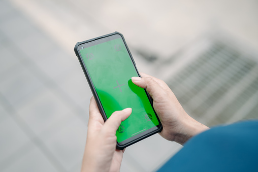 Female hands holding smartphone with green screen.