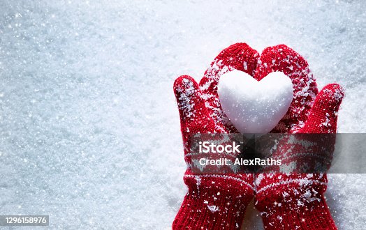 istock Female hands in knitted mittens with snowy heart against snow background 1296158976