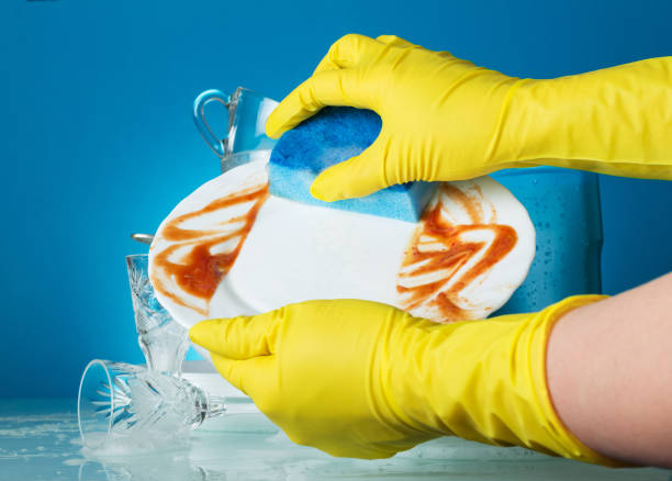 Female hands in yellow gloves wash a dirty plate on blue background stock photo