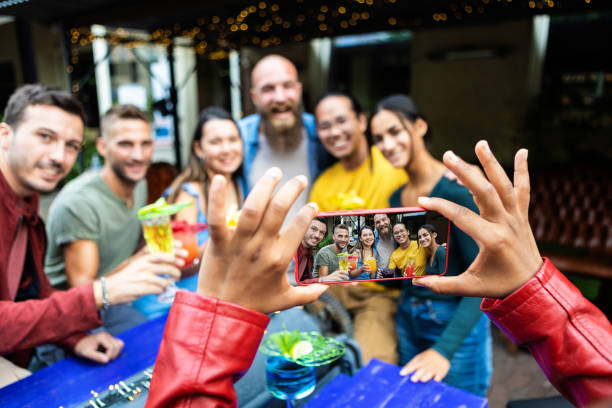Female hands taking photo with mobile phone of young friends at trendy pub stock photo