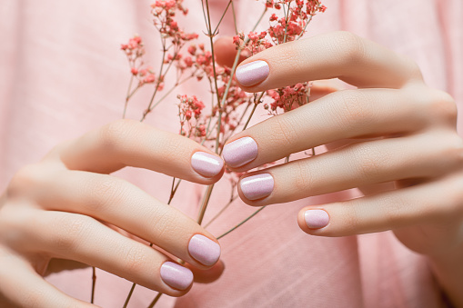 Female hands with pink nail design. Pink nail polish manicure. Woman hands hold orange flowers