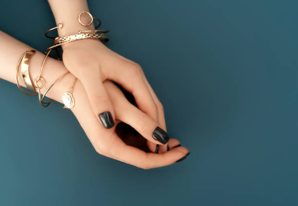 Female hands with trendy dark nail design with gold bracelets on aqua background. Luxury concept. Festive backdrop for your design. Female hands with trendy dark nail design with gold bracelets on aqua background. Luxury concept. Festive backdrop for your design. Top view. wristband stock pictures, royalty-free photos & images