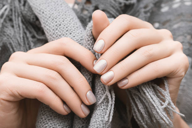 Female hands with white nail design. Glitter white nail polish manicure. Woman hands on gray wool scarf. stock photo