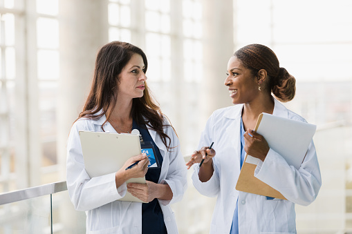 Two mid adult female healthcare professionals walk and talk together.