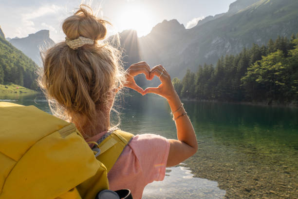 Female hiker makes a heart shape finger frame on the spectacular alpine landscape to show love to the environment concept stock photo