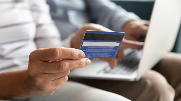 Female holding credit card making online payment, closeup view Close wife fingers holding plastic credit card on background computer on husband lap, old couple booking hotel using on-line app service and website, make online payment, shopping via internet concept white collar crime stock pictures, royalty-free photos & images