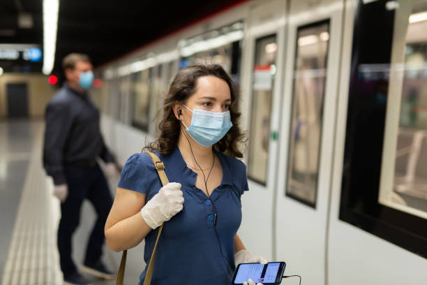 mulher com máscara facial e fones de ouvido na plataforma do metrô - máscara covid - fotografias e filmes do acervo