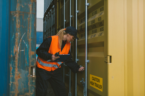 Female Manual worker  checking cargo containers in yard. Making  report of checked cargo containers and using walkie talkie