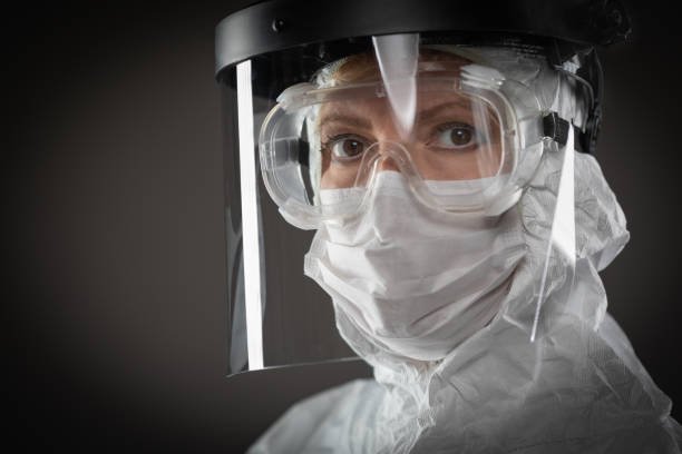 Female Medical Worker Wearing Protective Face Mask and Gear Against Dark Background Female Medical Worker Wearing Protective Face Mask and Gear Against Dark Background. clothing protection stock pictures, royalty-free photos & images