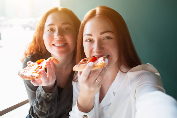 weibliche models machen ein selfie auf einem handy in caffee. junge frauen lächeln und essen pizza - vladmodels stock-fotos und bilder